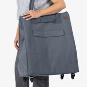 Person holding a large gray tote bag with wheels on a white background