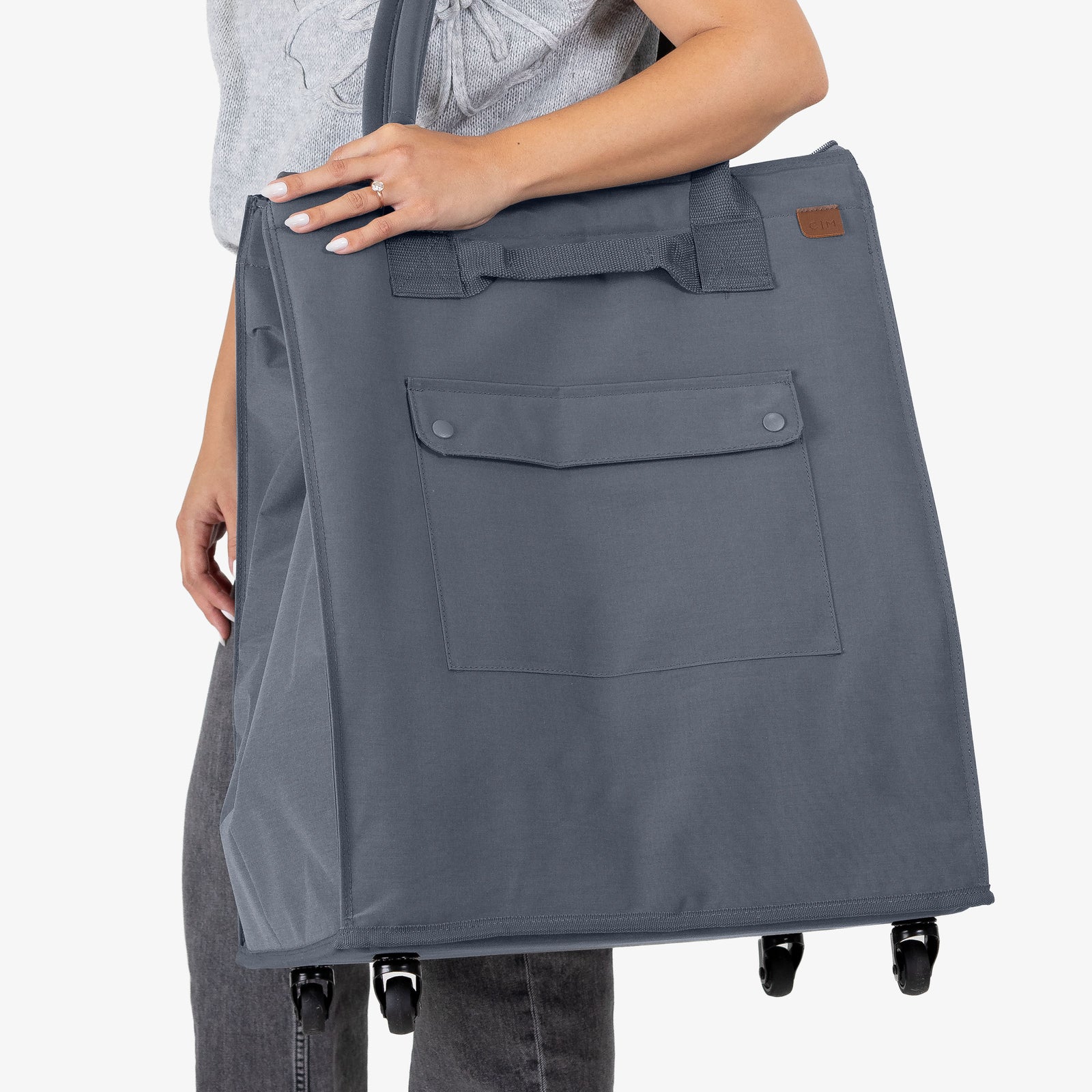 Person holding a large gray tote bag with wheels on a white background