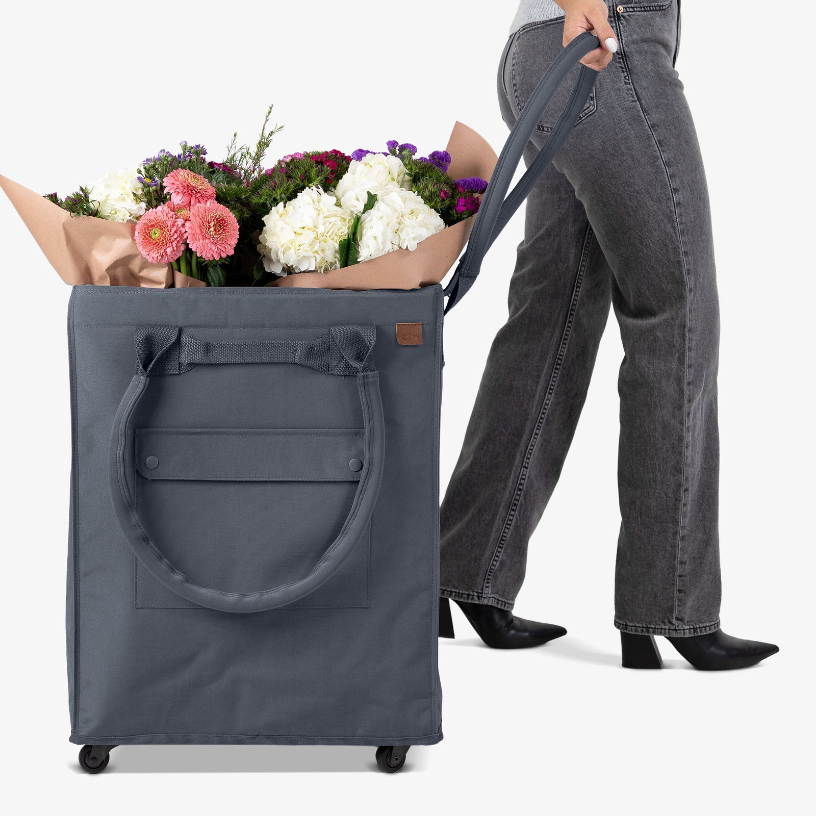 Person holding a large gray rolling bag filled with flowers on a white background