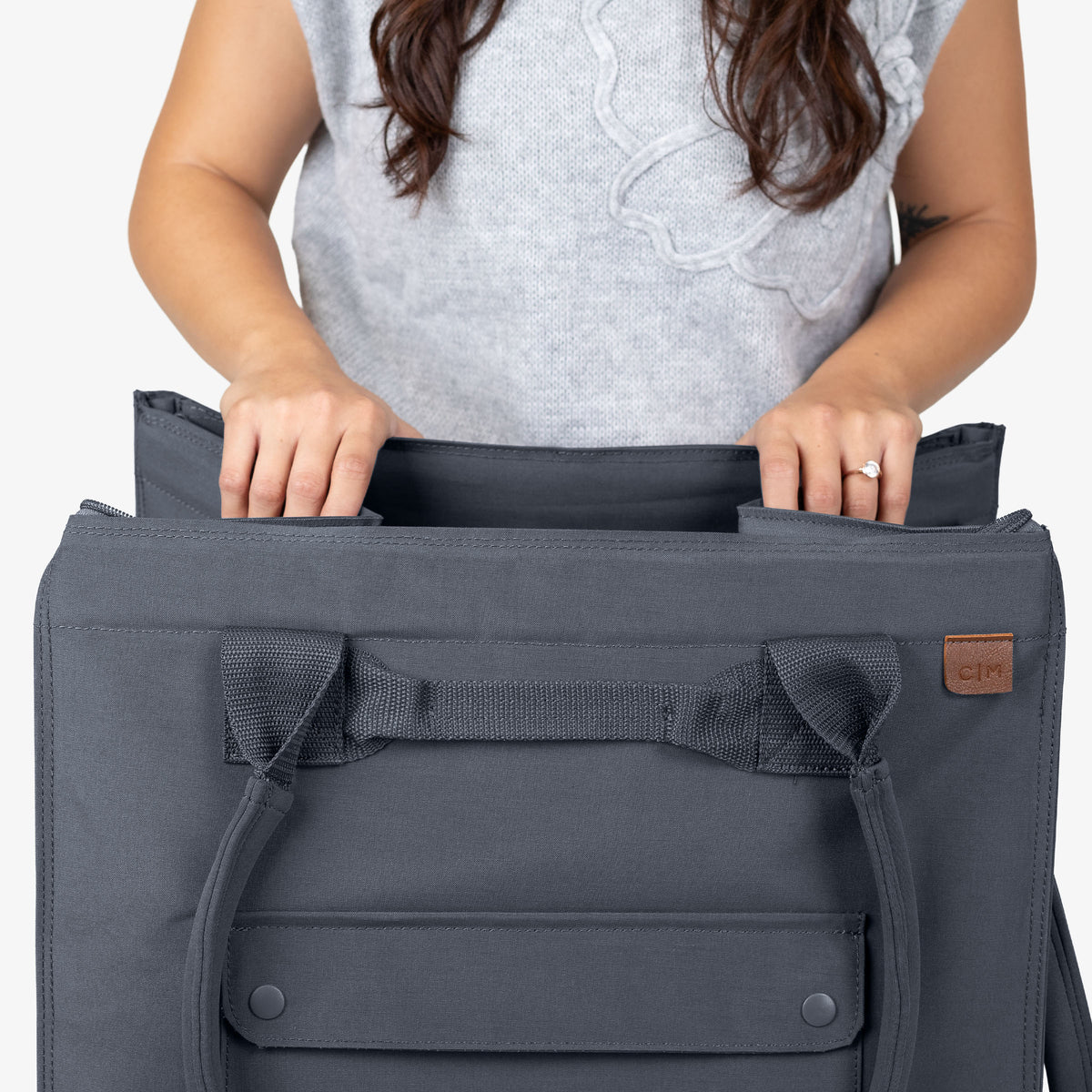 Person holding a gray bag with a visible brand logo on a white background
