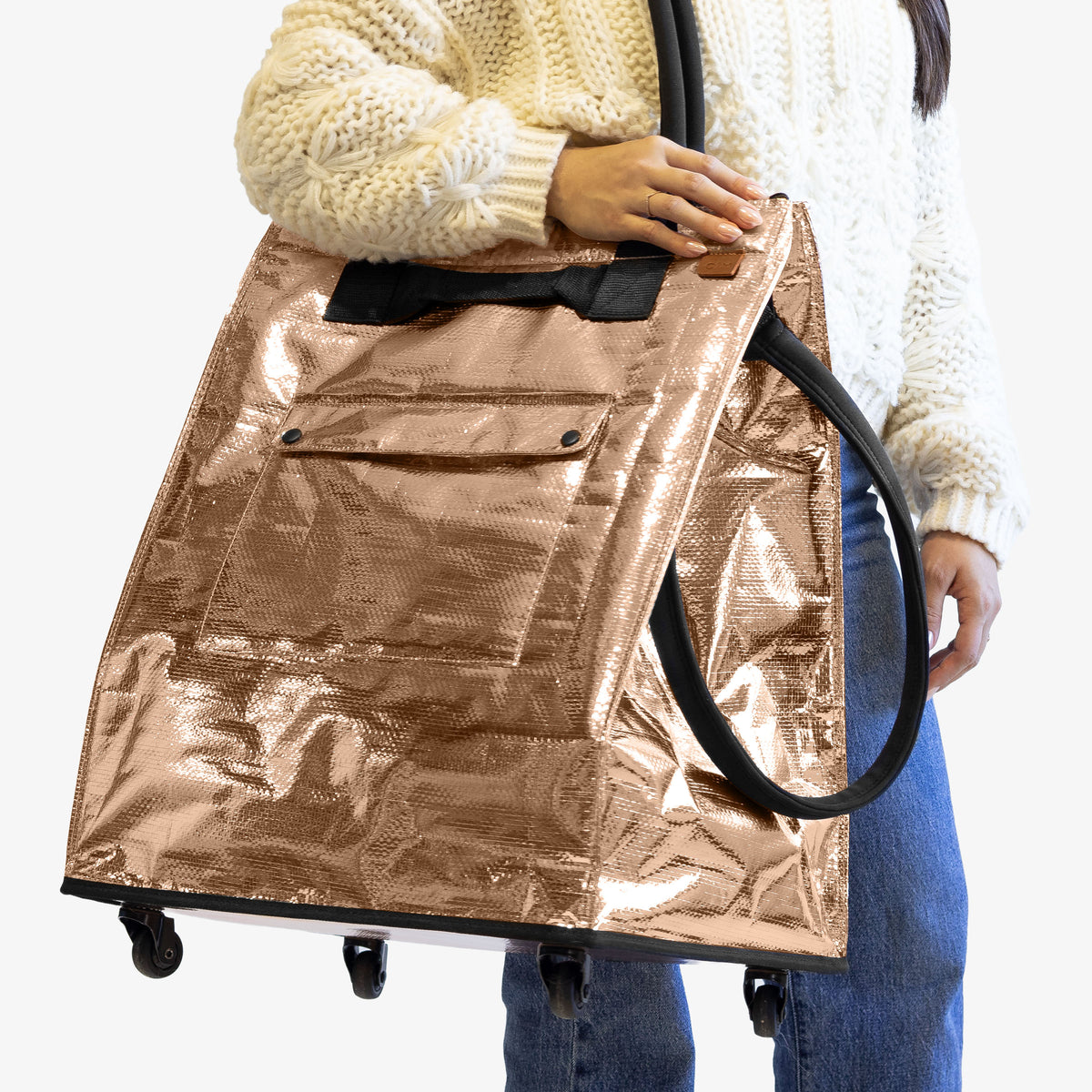 Person holding a large metallic gold bag with wheels on a white background