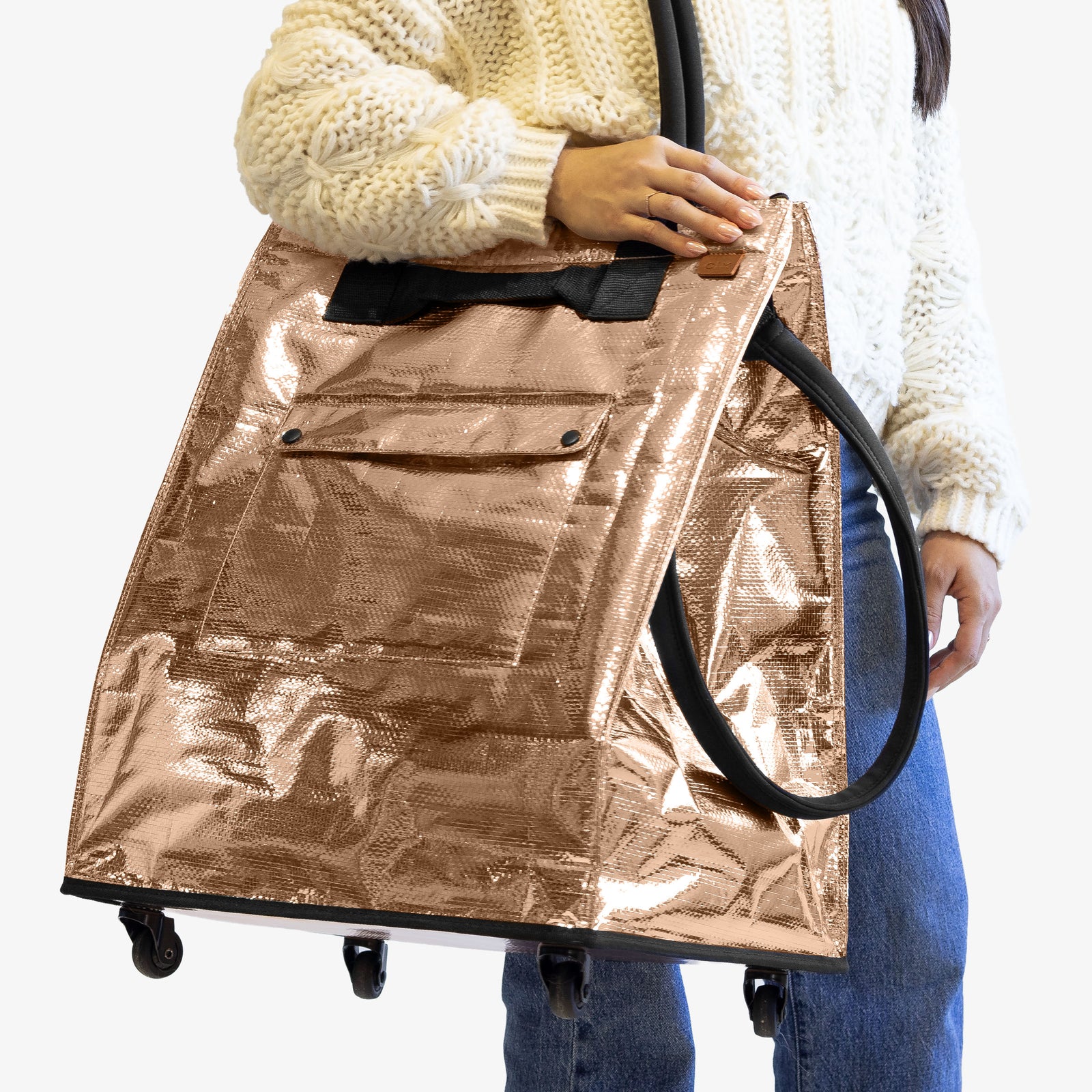 Person holding a large metallic gold bag with wheels on a white background