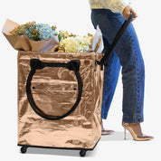 Person pulling a large metallic shopping bag filled with flowers on wheels.