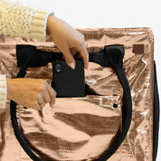 Person holding a black phone case over a rose gold metallic bag