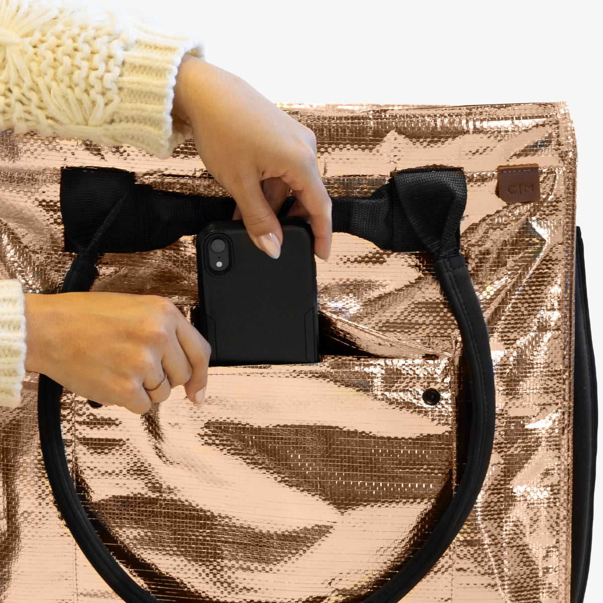 Person holding a black phone case over a rose gold metallic bag