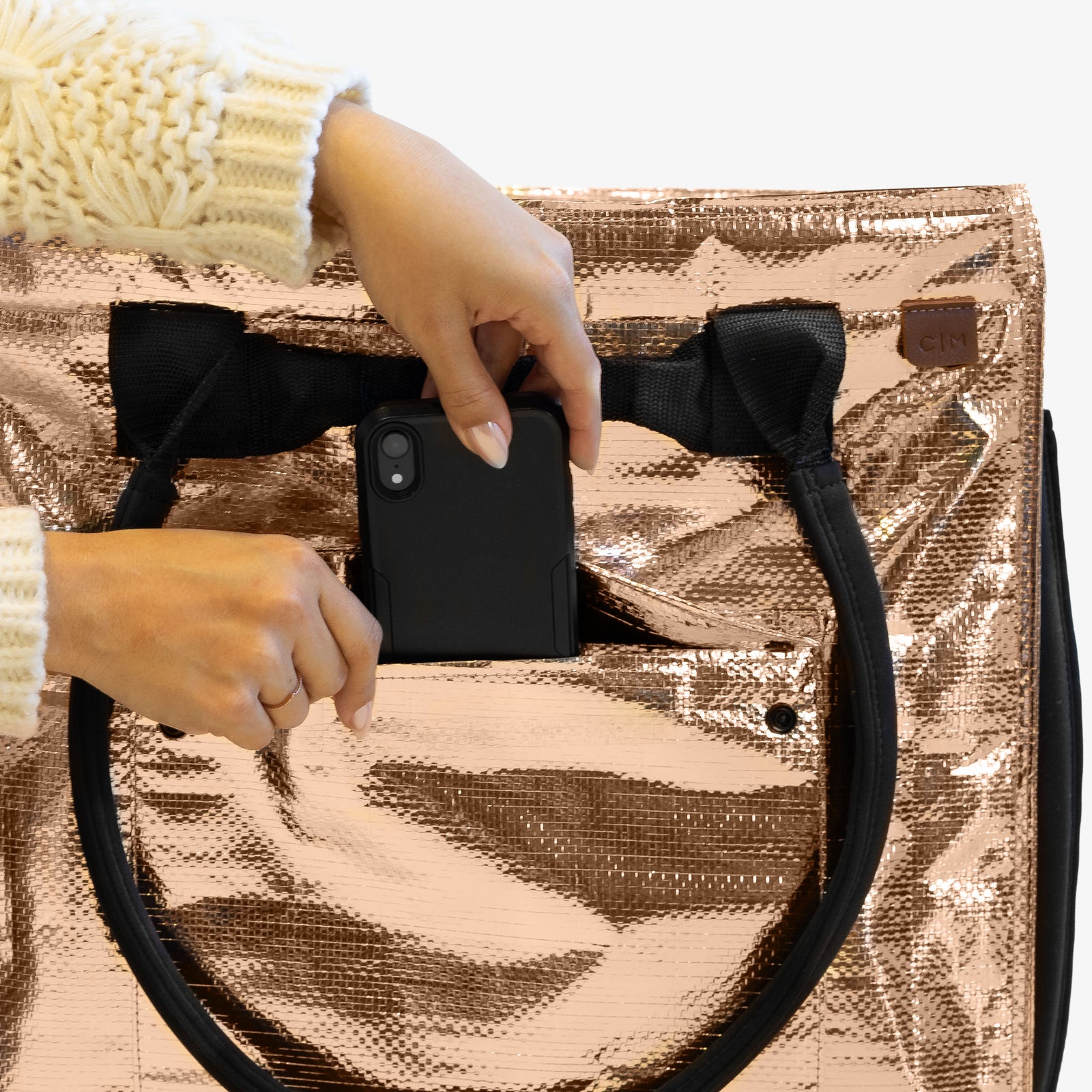 Person holding a black phone case over a rose gold metallic bag