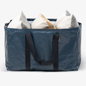 Blue storage bag with black handles filled with pillows on a white background