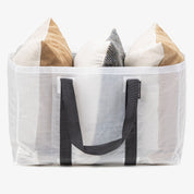 White mesh tote bag with black handles containing decorative pillows on a white background