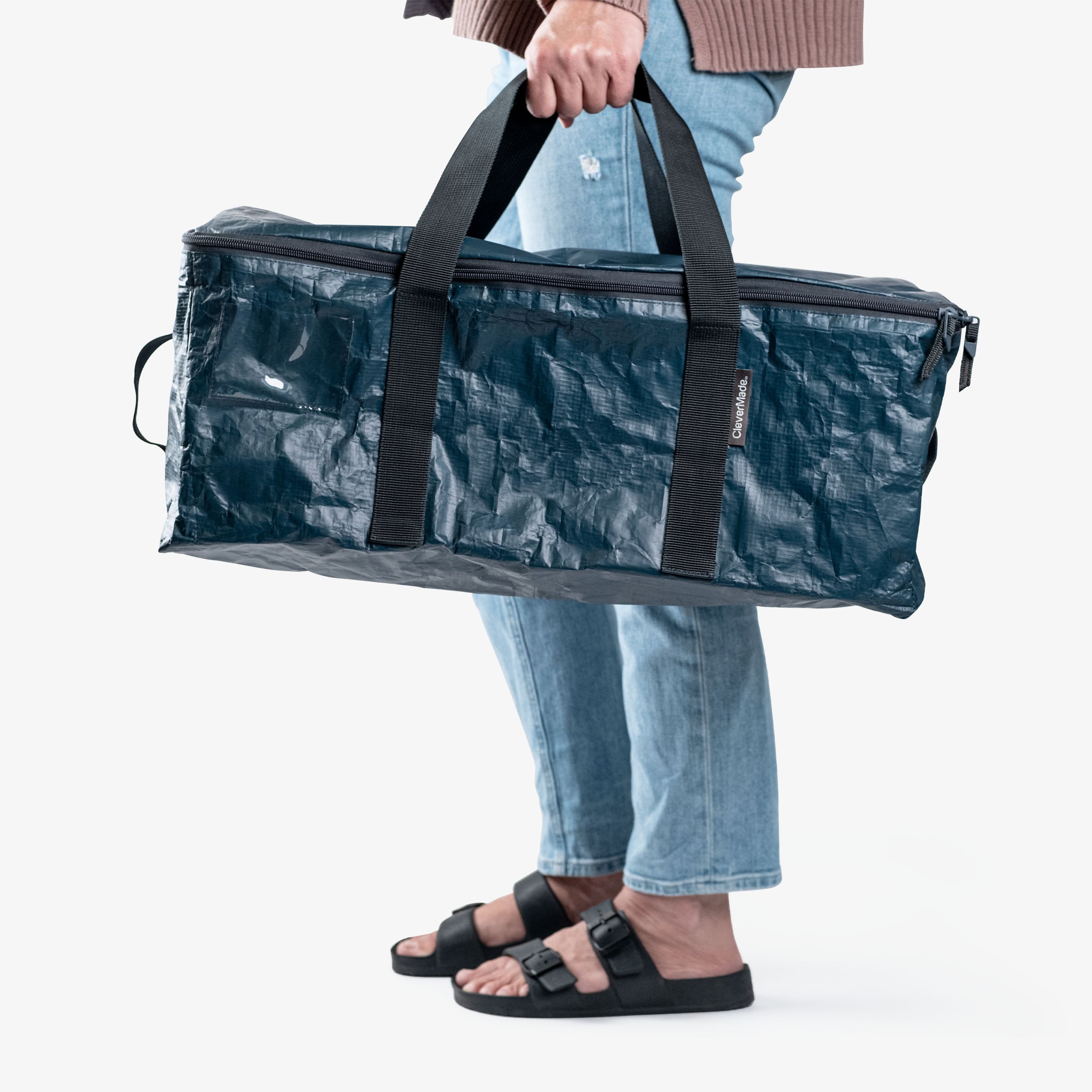 Person holding a blue storage duffel bag with black straps on a white background