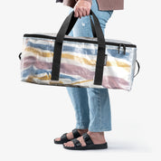 Person holding a large striped duffel bag with a transparent side panel on a white background