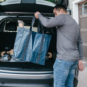 Man loading a blue reusable storage tote bag into the trunk of a car