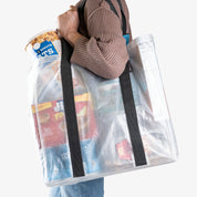 Person carrying clear reusable shopping bag with snacks on her shoulder