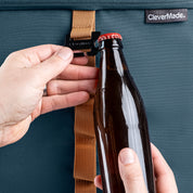 Person opening a bottle with a bottle opener attached to the blue cooler  bag, featuring the CleverMade brand.