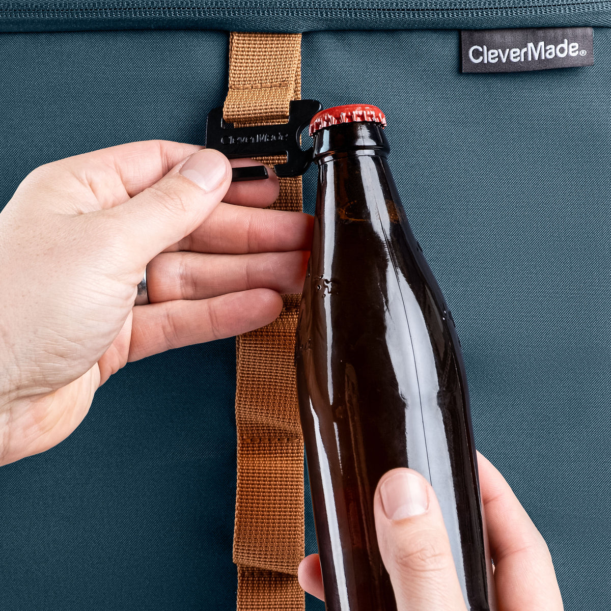 Person opening a bottle with a bottle opener attached to the blue cooler  bag, featuring the CleverMade brand.